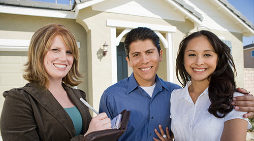 Happy young adult couple and house agent standing in front of the house photo